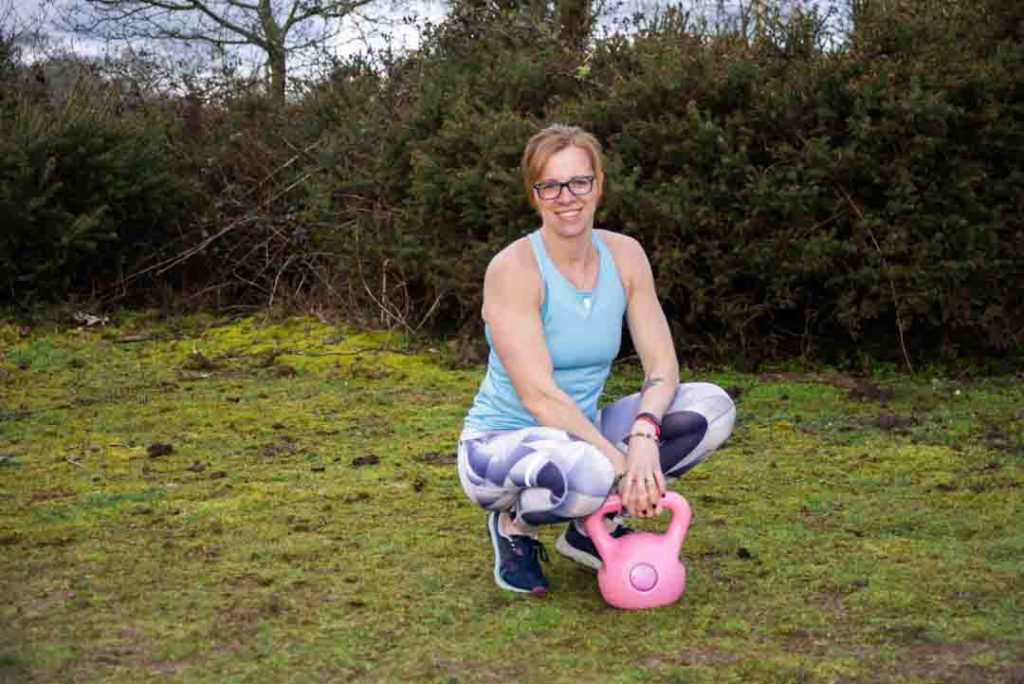 Women in the forest wearing sport clothes holding a kettlebell